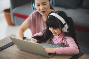 Asian parent mom and dad with female chid are listening to music with wireless headphones and laptop at home.