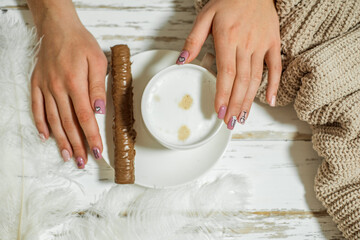 Woman's hands in sweater holding cup of coffee on wooden table.chocolate on a plate
