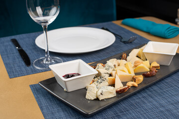 Assortment of cheese with honey, nuts and grape on a modern cutting board slate background
