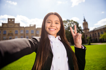 Photo of positive schoolgirl shoot selfie showing v-sign video call wear black uniform white shirt urban city outside