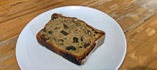 A piece of homemade coffee and walnut cake served in white plate on wooden table.