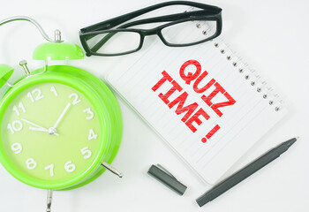 alarm clock,glasses,pen and notebook written quiz time over white background
