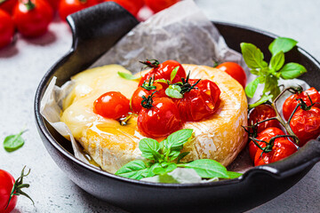 Baked Camembert or Brie cheese with tomatoes in black pan.