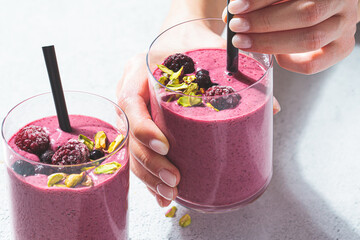 Berry smoothie with nuts in woman hands, light gray background. Healthy detox drink concept.