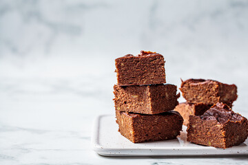 Stack of vegan brownies with dark chocolate on white board, white background, copy space. Vegan...