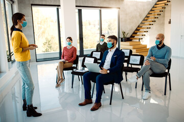 Female entrepreneur talking to her colleagues while giving them business presentation during COVID-19 pandemic.