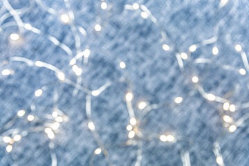Glowing bokeh from a garland on a blue denim background. Christmas light, magic, glitter, celebration. A universal beautiful background with blur in gentle colors. Background for websites, designers.