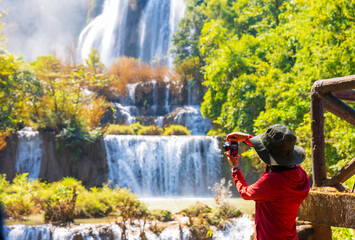 Asian woman taking a photo of Beautiful waterfall (Thi Lor Su) in Tak, Thailand.