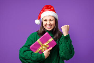happy young woman in Christmas cap with gift on purple background