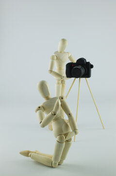 Wooden artist manikin taking a photograph of a mannequin posing for the camera, isolated on plain background with copy space in vertical format