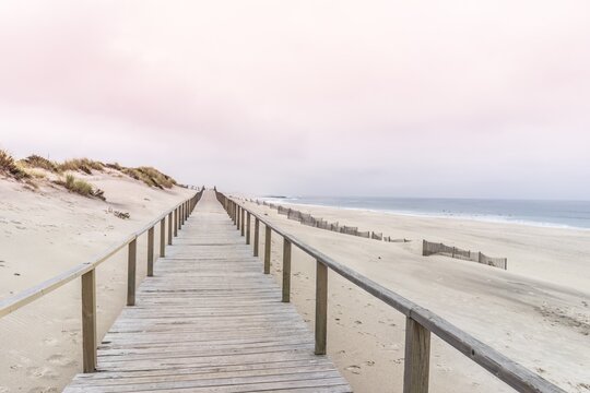 Diminishing Perspective Of Boardwalk At Beach Against Cloudy Sky