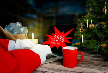 santa is checking 25 percent winter sale advertising on laptop in his workshop