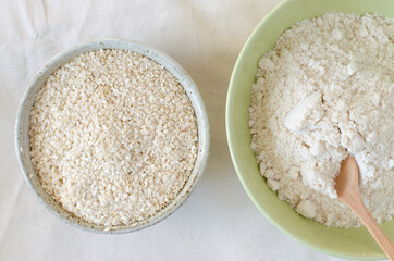 Squeezed white sesame and sesame flour in bowls on linen background. Benne oilcake. Top view.