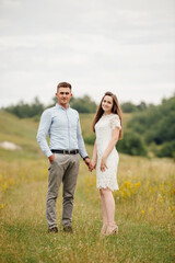 Young beautiful couple hand by hand walking in the field in summer. woman with long hair and man with stylish haircut.
