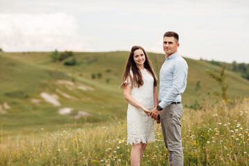 Young beautiful couple is hugging in the field in summer. woman with long hair and man with stylish haircut