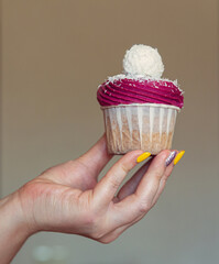 cupcake with white cream decorated with coconut and almond candy in the hand of a woman
