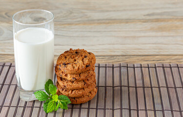 A stack of chocolate chips cookies on baking paper, with a glass of milk on a light wooden background