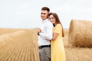 Photo of joyful couple man and woman walking through golden field with bunch of haystacks and hugging together during sunny day