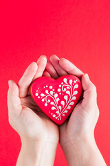 Gingerbread in the form of a heart with a beautiful pattern in female hands on a red background, place for text, top view, valentines day