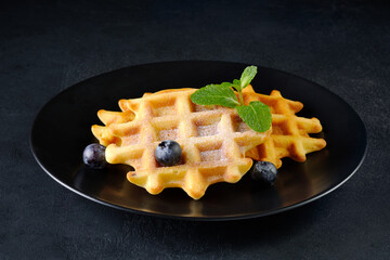 Delicious belgian waffles with blueberries and mint on black background