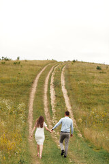 Naklejka premium rear view of Young beautiful couple hand by hand walking in the field in summer. woman with long hair and man with stylish haircut