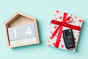 Fototapeta na wymiar Top view of car key on a gift box with red hearts and festive calendar on colorful background. The fourteenth of february. Present for Valentine's Day concept