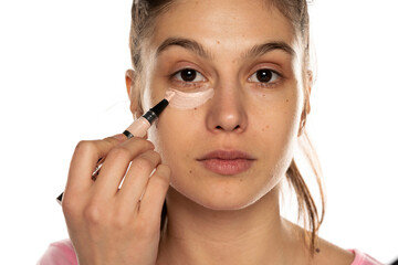 Portrait of young beautiful woman applying concealer with brush