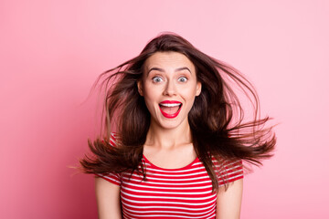 Portrait of young attractive smiling excited shocked girl open mouth flying hair isolated on pink...