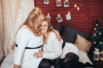 Mom and daughter are sitting on the big bed. Christmas mood. Against the background of a brick wall with garlands