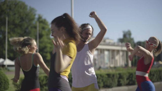 Young handsome 1980s man with retro tape recorder moving and singing as group of slim beautiful Caucasian women dancing around. Disco music and lifestyle concept.