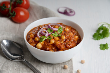 Chole masala also known as channay, chana is an indian street food made of chickpeas, chopped tomatoes, ghee and cumin decorated with red onion rings and parsley served in bowl with spoon on textile