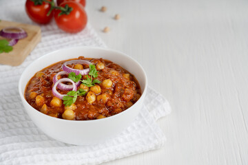 Chole masala as well as channay, chana is an indian street food made of chickpeas, chopped tomatoes and cumin decorated with red onion rings and parsley in bowl on textile. Image with copy space