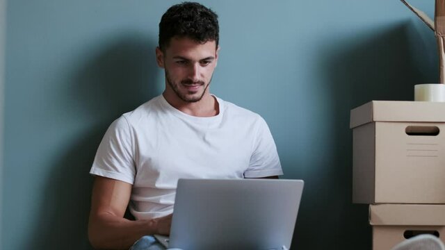 Video of handsome young man working with computer while taking a break sitting on the floor at home.