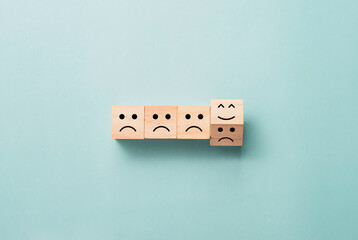 Flipping of wooden cube block from sad to smile emotion on blue background.