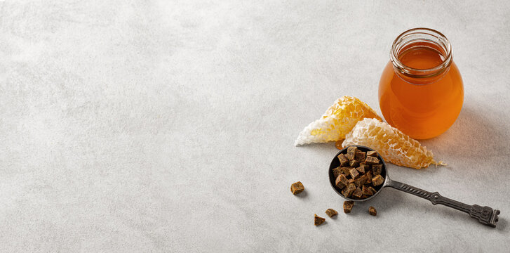 Honey background. Honey in a glass jar, honeycomb and propolis in an iron spoon. Light gray background. Banner.