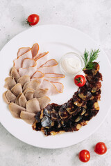 Meat and sausage slices on a plate with garlic sauce and cherry tomatoes, restaurant dish