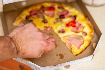 Pieces of pizza in a cardboard box. The man's hand reaches out.