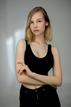 Portrait of a casual blonde woman in black top and jeans on gray background,crossed her arms on her chest