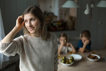 Girl in the kitchen looking to side, against the background of boys at table.
