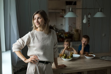 Girl in the kitchen looking to side, against the background of boys at table.