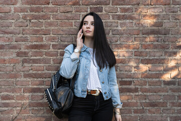 Female student with black hair and freckles leaning against a brick wall while talking on the phone