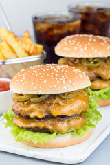 Homemade double cheese burger with two beef patty, cheddar cheese, lettuce, caramelized onion and jalapeno slices, served with french fries and soda, vertical