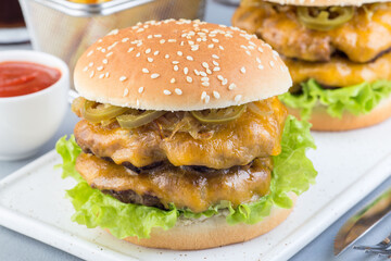 Homemade double cheese burger with two beef patty, cheddar cheese, lettuce, caramelized onion and jalapeno slices, served with french fries and soda, horizontal, closeup