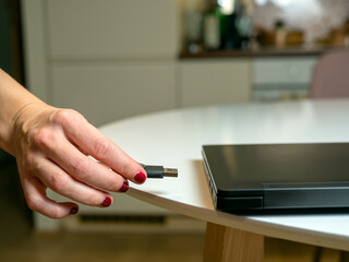 female manicured hand plugging usb, connecting USB flash drive in white laptop, kitchen in a flat. Plugging removable flash disk. Woman hand is using the USB while working at home during Covid-19