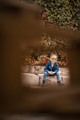 A cute little girl is sitting in sunglasses on a stone fence. Stylish child in a blue jacket. Casual style, fashion for children, fashionable suit, happy childhood