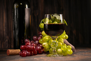 Red wine in glass with vintage bottle and with bunch of red and white grapes on wooden background