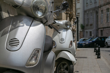 Close-up of two silver vintage scooters parked on sidewalk of empty quiet city street at summer day, rental small motorbikes for tourist destination, urban transport 