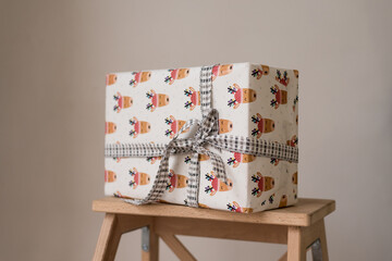 A gift in box wrapped in festive paper and tied with satin ribbon with a bow. On lilac background, copy space
