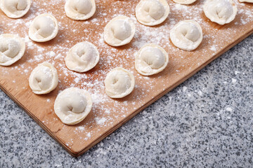 Fototapeta na wymiar Raw ravioli (or dumplings) on wooden board on stone table.