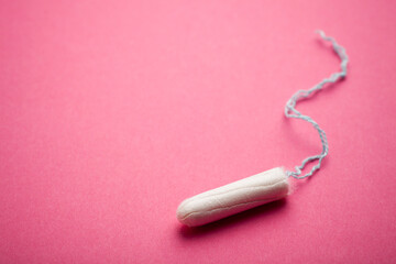 White tampon with light blue string on a colorful pink background. Shallow depth of field.